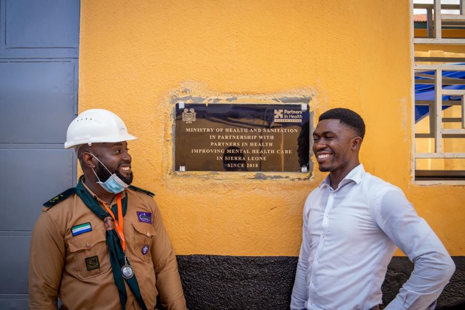 Sheriff and Alpha Sesay, who supervised the infrastructure remodel of SLPTH, pose with another plaque at the hospital. It reads: "Ministry of Health and Sanitation in partnership with Partners In Health, improving mental health care in Sierra Leone since 2018."