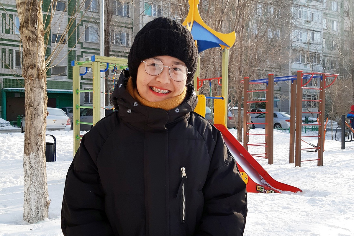 Maya, a patient in Kazakhstan who accessed tuberculosis care through Partners In Health and the endTB project, stands outside of a playground in a black winter hat and coat.
