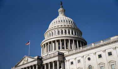 the U.S. Capitol building against a blue sky with an American flag blowing in the wind