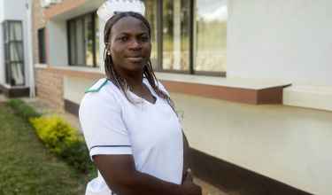 Chisomo Kondowe wears a white nurses uniform and stares directly at the camera. She stands outside of a beige building.