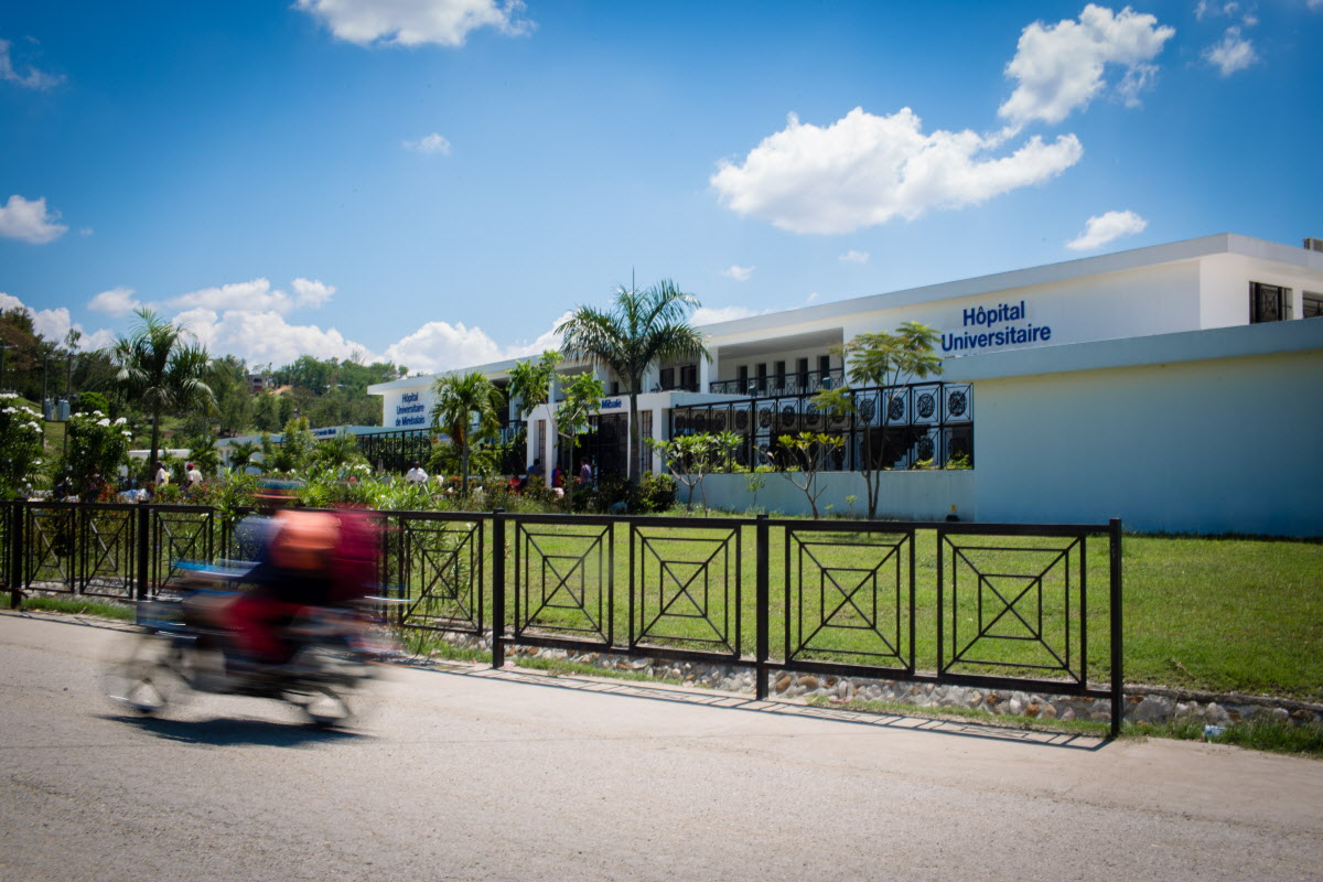 A scooter zooms by the wrought iron gates preceding University Hospital in Mirebalais, Haiti.