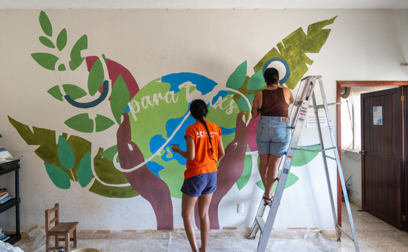 Marina Luria (left) and Diana Bernal (right) paint a mural at the Companeros En Salud office in Jaltenango, Mexico