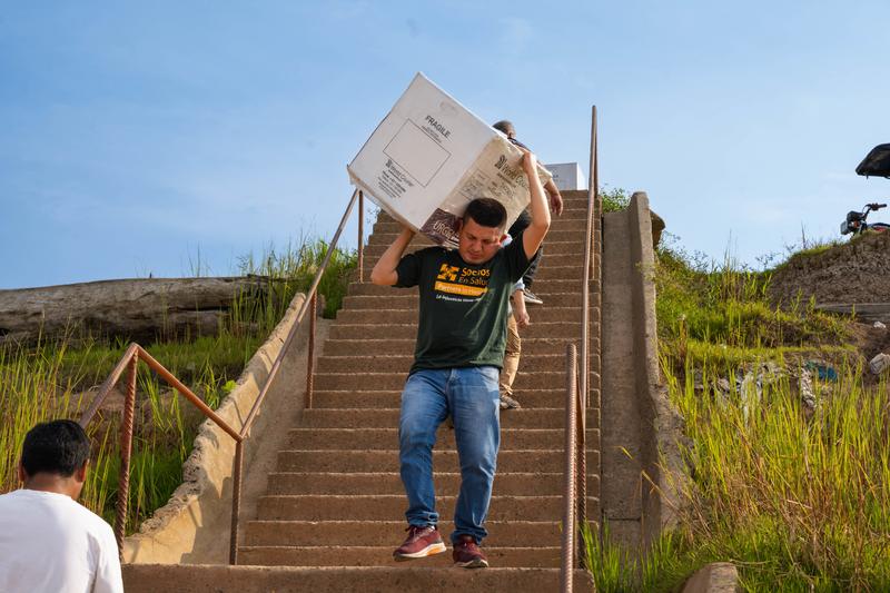 A Socios En Salud worker carries equipment for tuberculosis screening down a flight of stairs outside