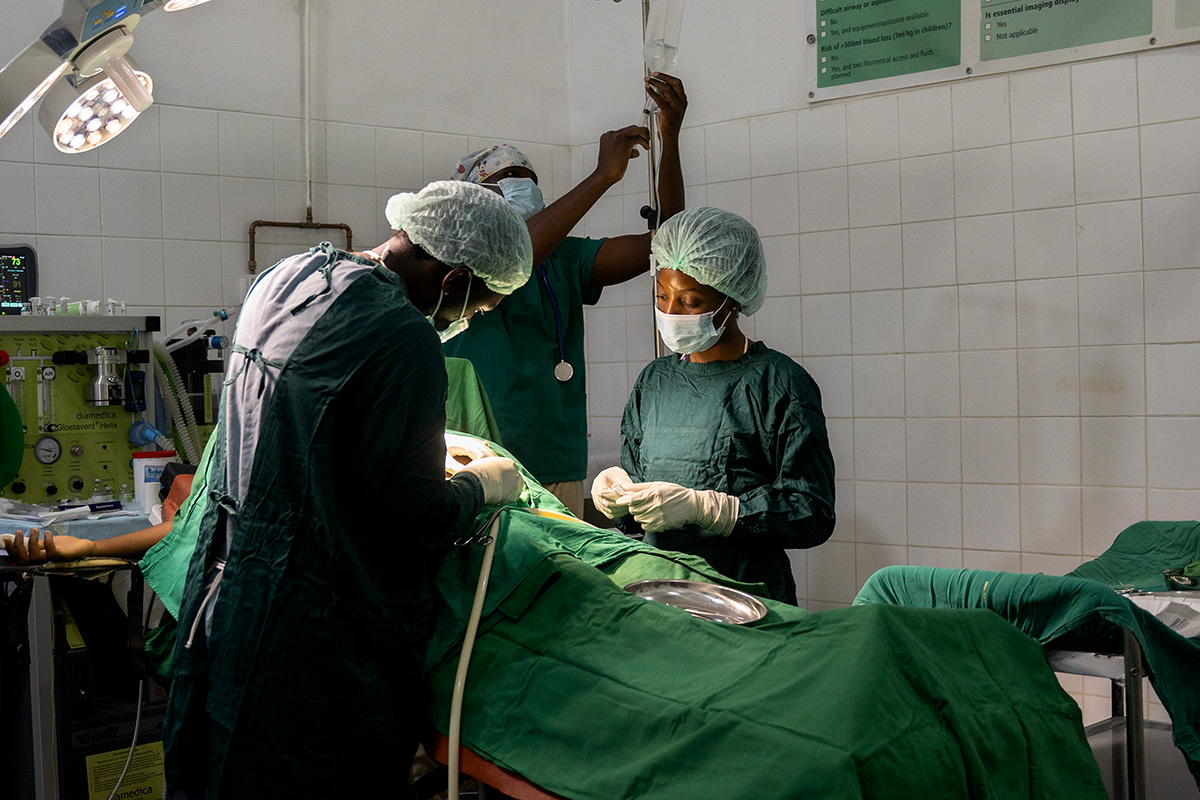 Doctors and nurses in green scrubs stand around a hospital bed as they perform a C-section on a patient.