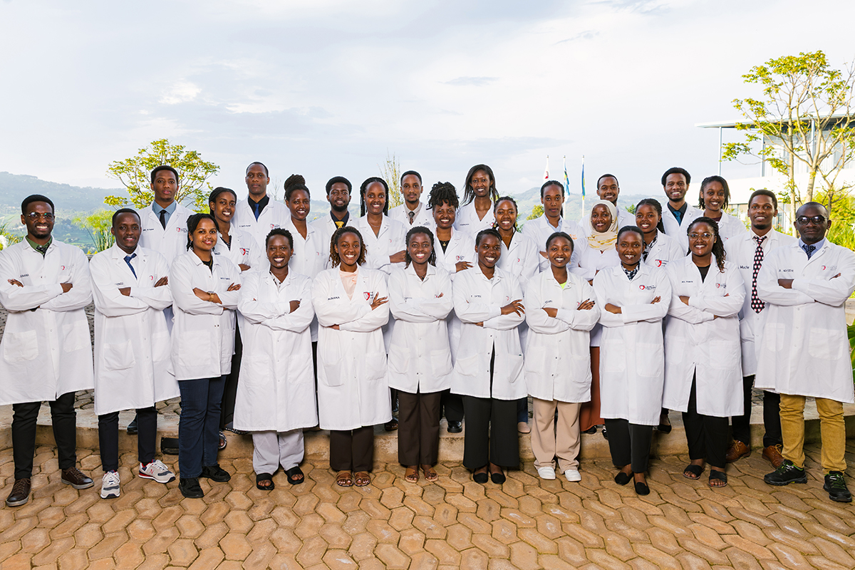 A group of 30 students in white lab coats stand in a group outside on the University of Global Health Equity campus.
