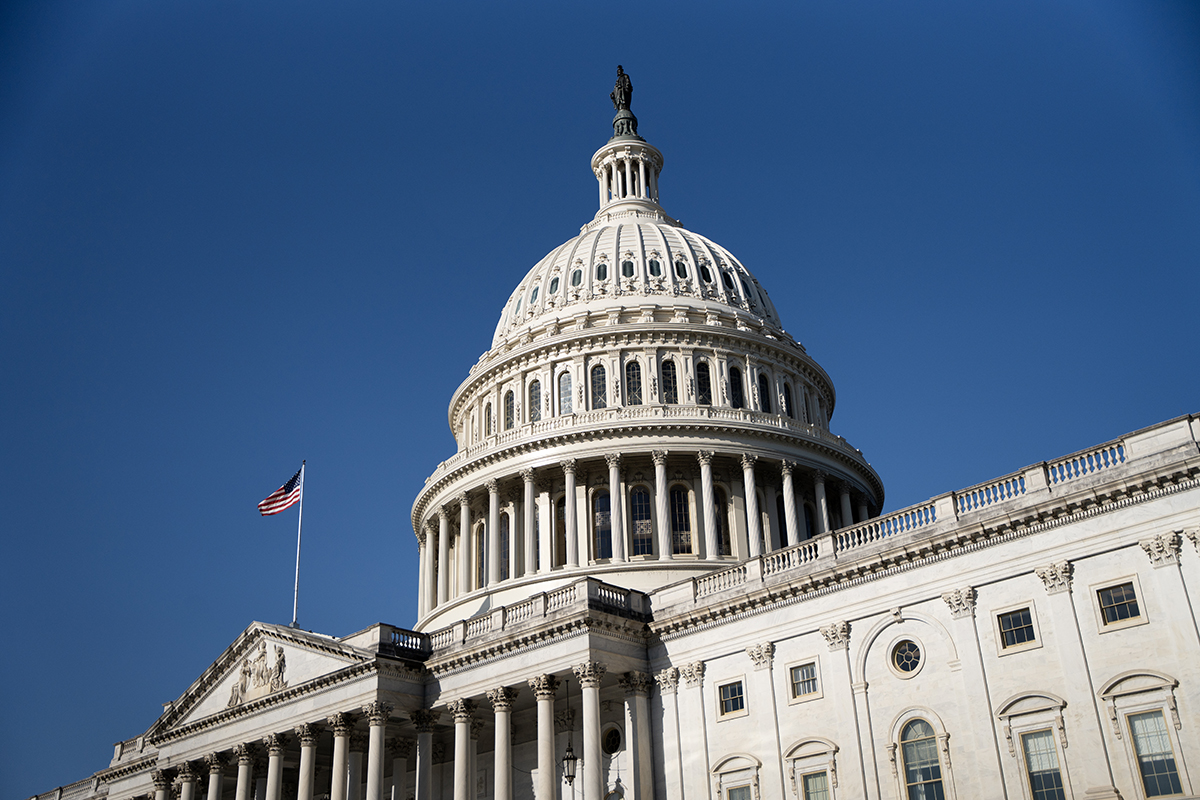 the U.S. Capitol building against a blue sky with an American flag blowing in the wind