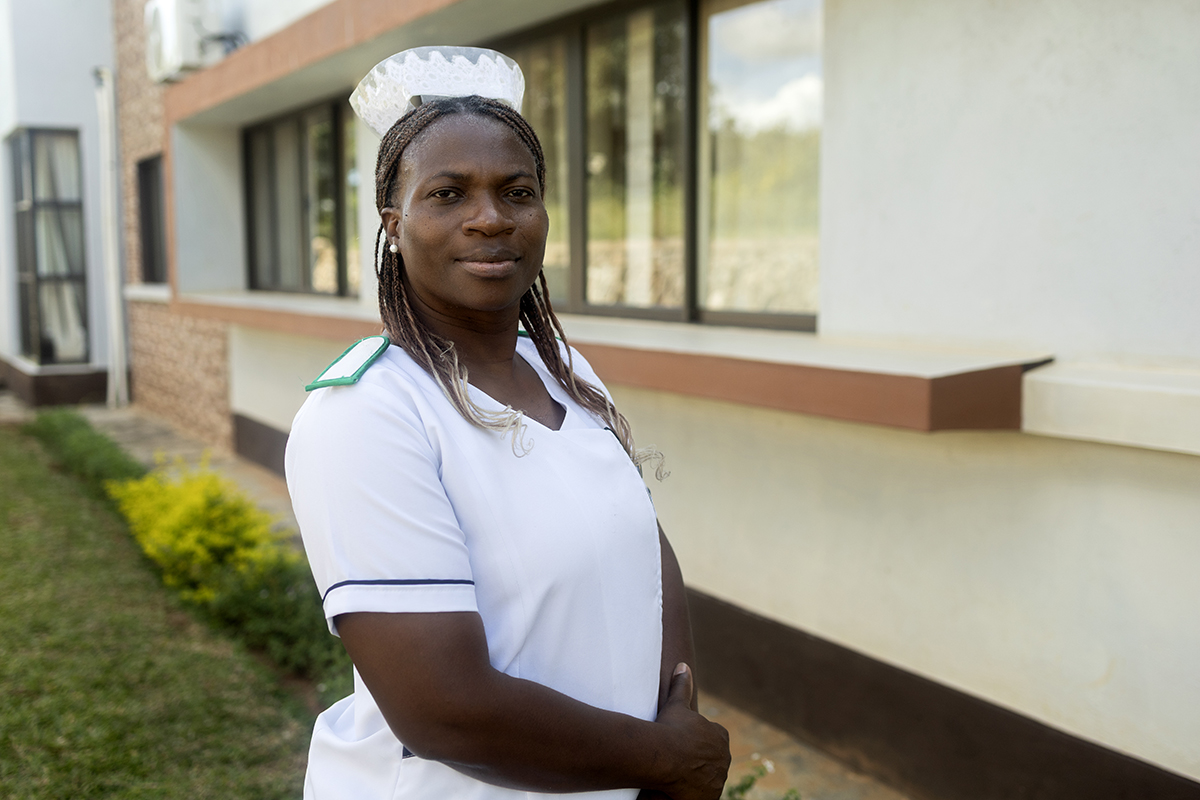 Chisomo Kondowe wears a white nurses uniform and stares directly at the camera. She stands outside of a beige building.