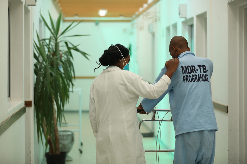 Tlotlisang Thai, registered nurse in the MDR-TB ward, walks with patient Thoriso Daniel Limo, who accessed treatment and care for HIV and MDR-TB through Partners In Health in Lesotho in 2019. Photo by Karin Schermbrucker for PIH.