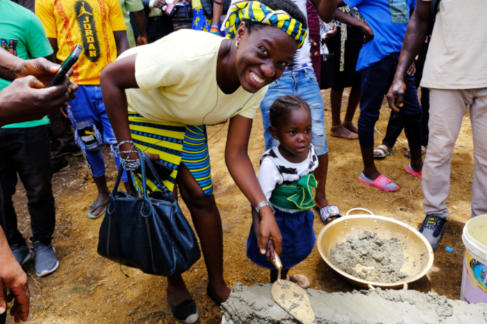 Two-year-old Esther Williams lays an MCOE brick with PIH physician Dr. Aramide Oteju