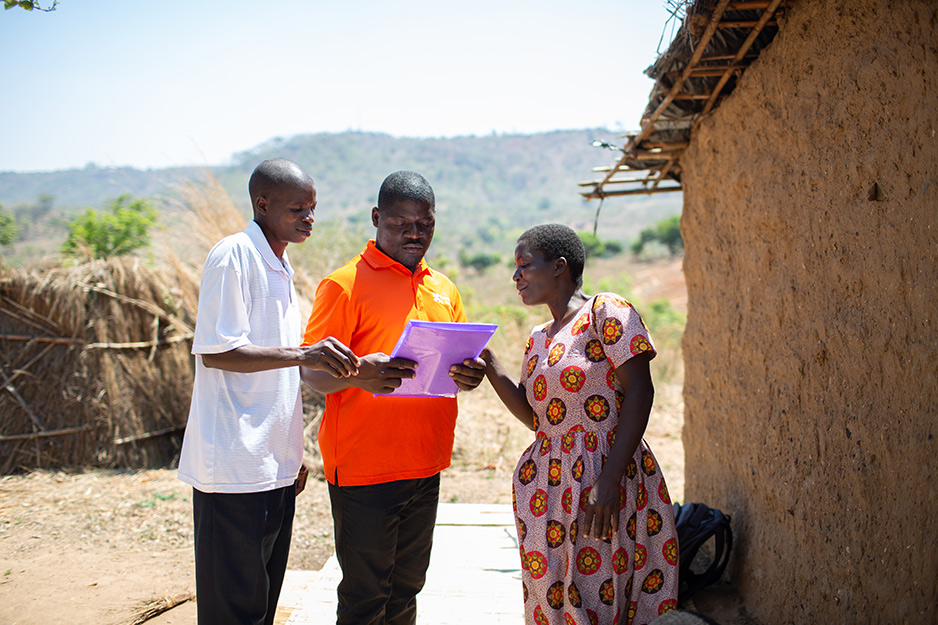 CHW site supervisor John Kaiya (left), CHW program manager Benson Chabwera and CHW Rose Zingwani review health documents for Agnes Paulo, a single mother living with HIV, at Paulo's home in Chinyani Village. 