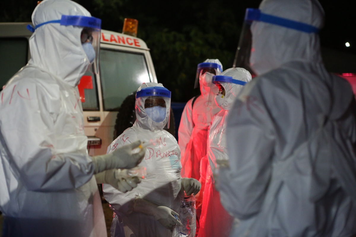 Clinicians in PPE stand outside of an ambulance and prepare to help patients at a triage area in Sierra Leone during the Ebola outbreak in 2015.