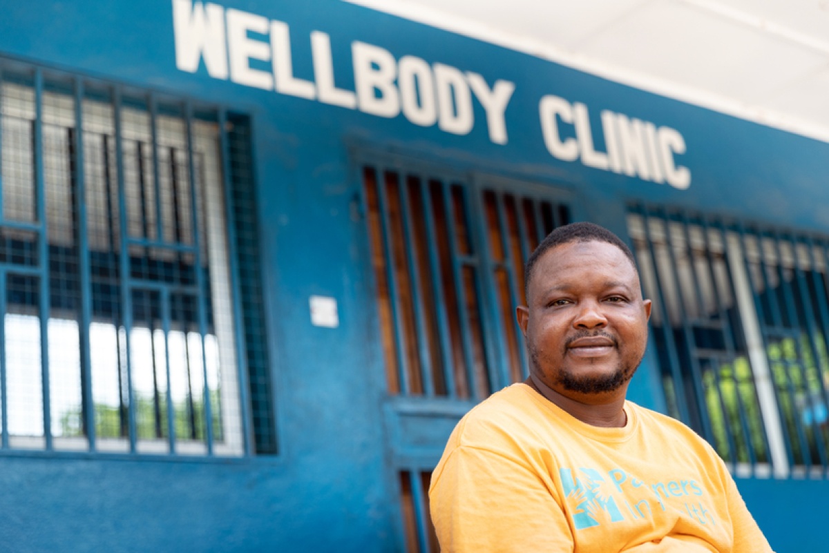 Bailor in an orange PIH t-shirt sitting in front of Wellbody Clinic