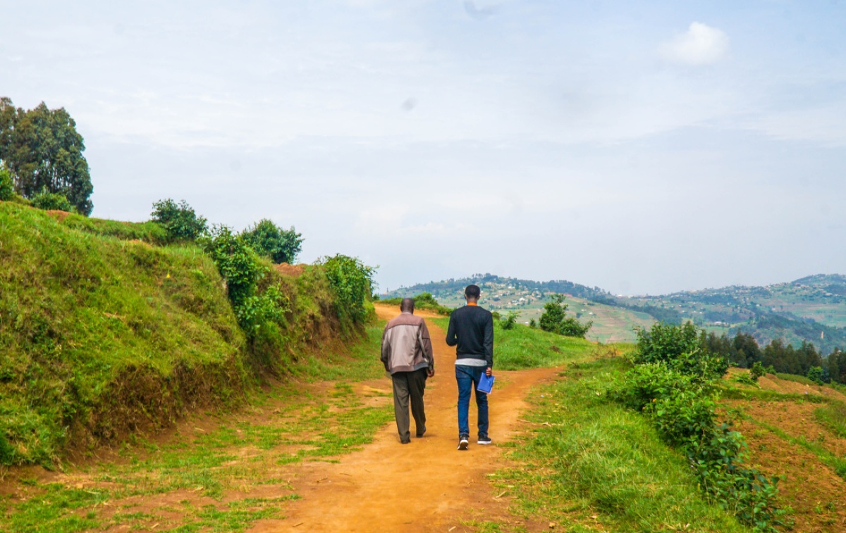 Eddy Mukwiza, livelihood program coordinator with Inshuti Mu Buzima, (right) walks with farmer Sylvien Gakwenza (left)