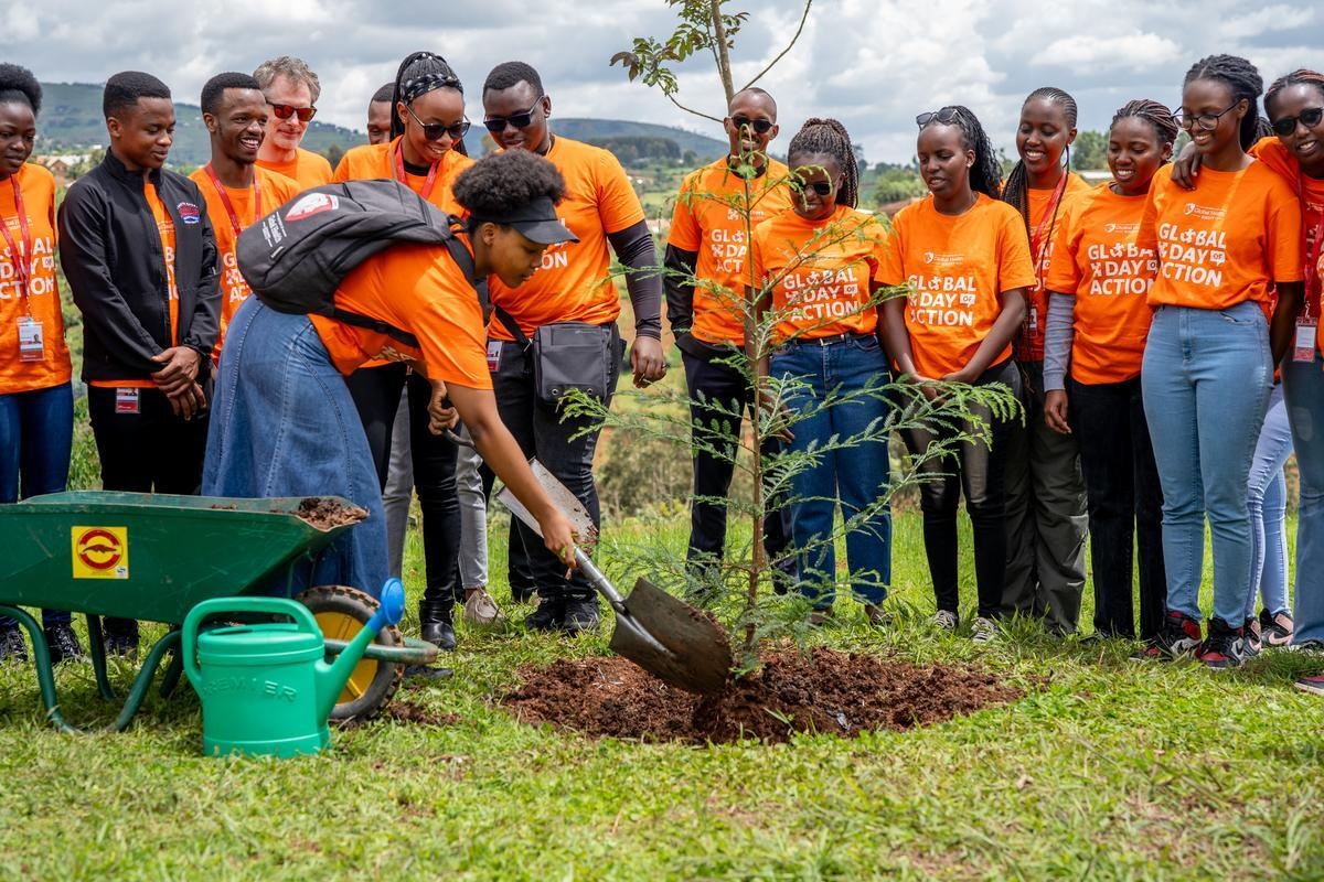 In Rwanda, a group of students, faculty, and staff wearing bright orange shirts that say "Global Day of Action" plant a coastal redwood tree in honor of Paul Farmer.