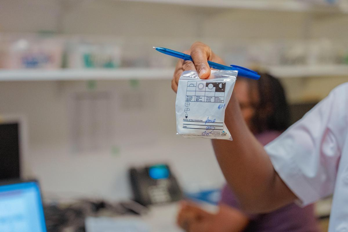 a hand with a blue pen holds up a small white plastic bag containing medication