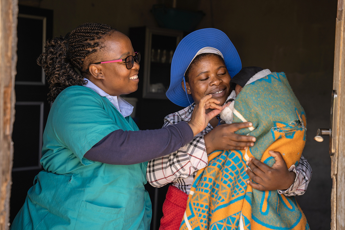 Mother holding baby, alongside clinical staff member in Lesotho