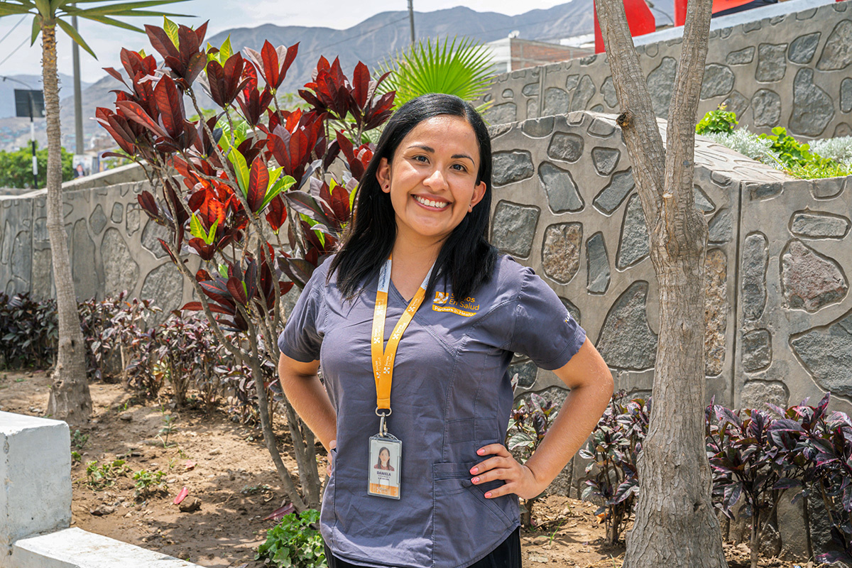 Daniela Puma Abarca smiles, facing the camera, wearing a grey polo and an orange lanyard in front of a stone wall