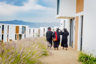 Three graduates in caps and gowns walk on UGHE's Butaro campus.