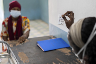 Medication in a small bag is being handed to a patient who sits across a table