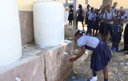 a girl washes her hands with soap and water at a school in Mirebalais, Haiti