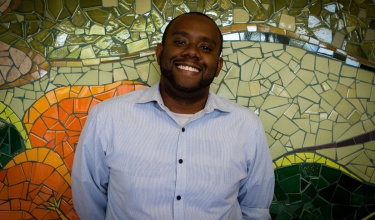 Dr. Lormil stands in front of mosaic wall 