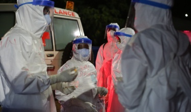 Clinicians in PPE stand outside of an ambulance and prepare to help patients at a triage area in Sierra Leone during the Ebola outbreak in 2015.