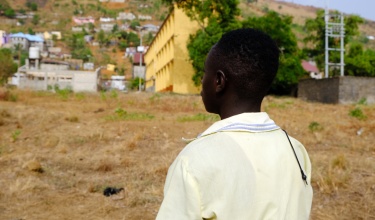 Hassan (name changed) stands in a light yellow shirt with his back to the camera for confidentiality.