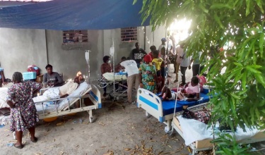 Injured people are treated under a tarp in a field hospital