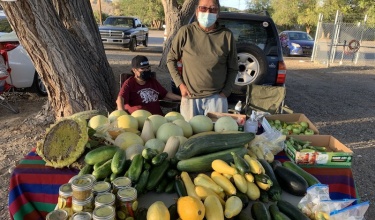 farmer stands behind table with produce at farmers market