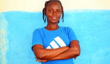 Tina Thomas stands with arm crossed in front of blue wall