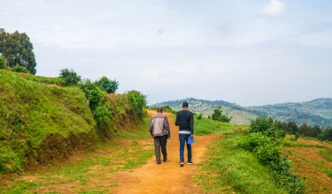 Eddy Mukwiza, livelihood program coordinator with Inshuti Mu Buzima, (right) walks with farmer Sylvien Gakwenza (left)
