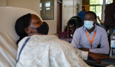 Uwimana Marie Gorethe speaks with oncology program manager Jean Bosco Bigirimana as she rests in bed at Butaro District Hospital, where she receives chemotherapy treatment.