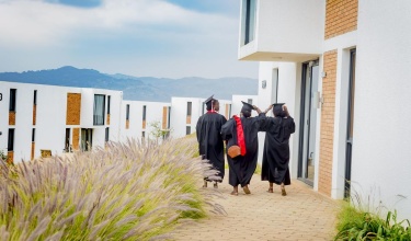 Three graduates in caps and gowns walk on UGHE's Butaro campus.