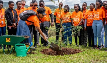 In Rwanda, a group of students, faculty, and staff wearing bright orange shirts that say "Global Day of Action" plant a coastal redwood tree in honor of Paul Farmer.