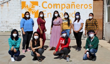 Ten women wearing face masks stand outside of a wall that says Compañeros En Salud, as Partners In Health is known in Mexico. Photo by Francisco Terán / Partners In Health.