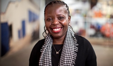Basimenye Nhlema smiles at the camera in a black shirt with a black and white scarf