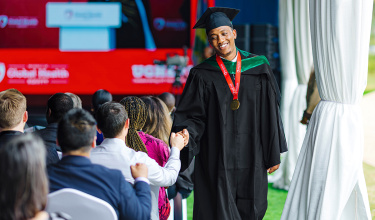 Graduate Heritier Mfura, class representative for the inaugural MBBS-MGHD cohort, fist bumps an audience member.